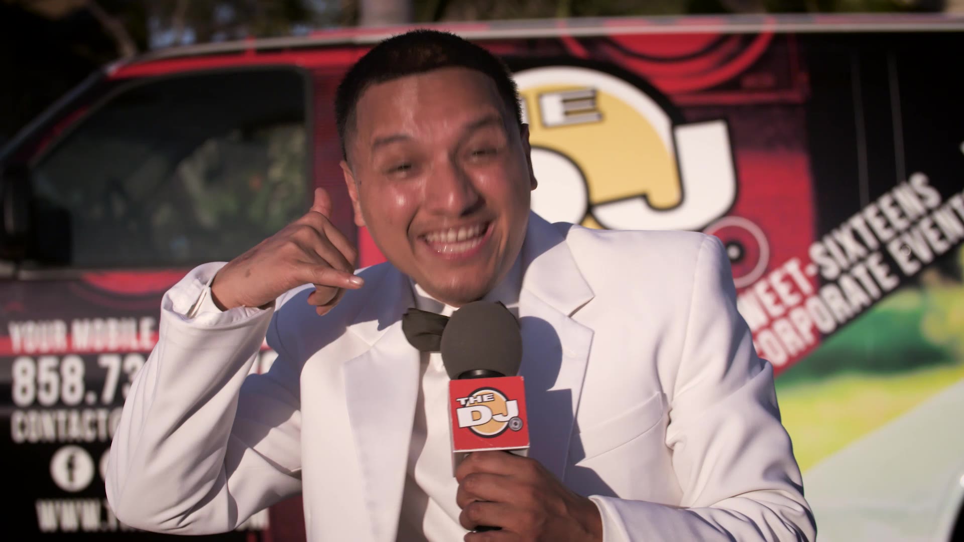 The DJ making a call-me gesture beside the van showing 858-735-5279