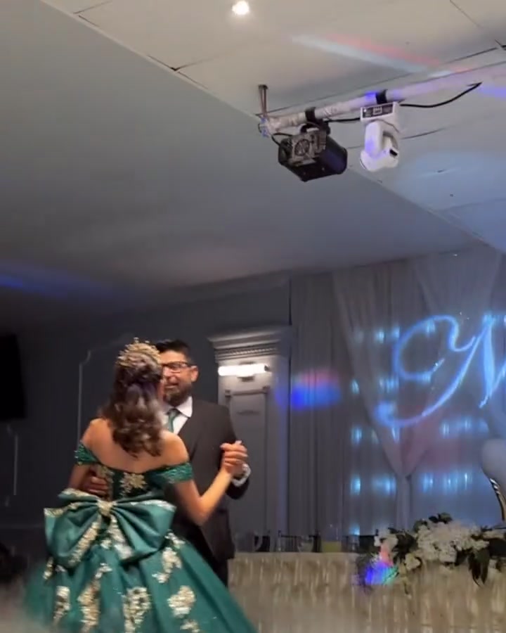 Quinceañera in an emerald gown with a large bow dancing with her father